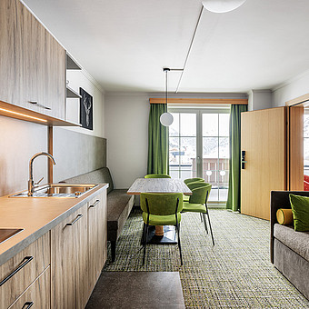 Eine Küche, ein Esstisch eine Couch und ein Fernseher in einem modernen Apartment.
