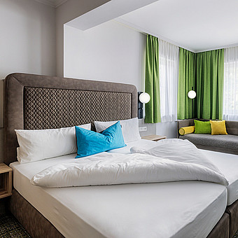 Neben einem großen Doppelbett steht eine Couch.