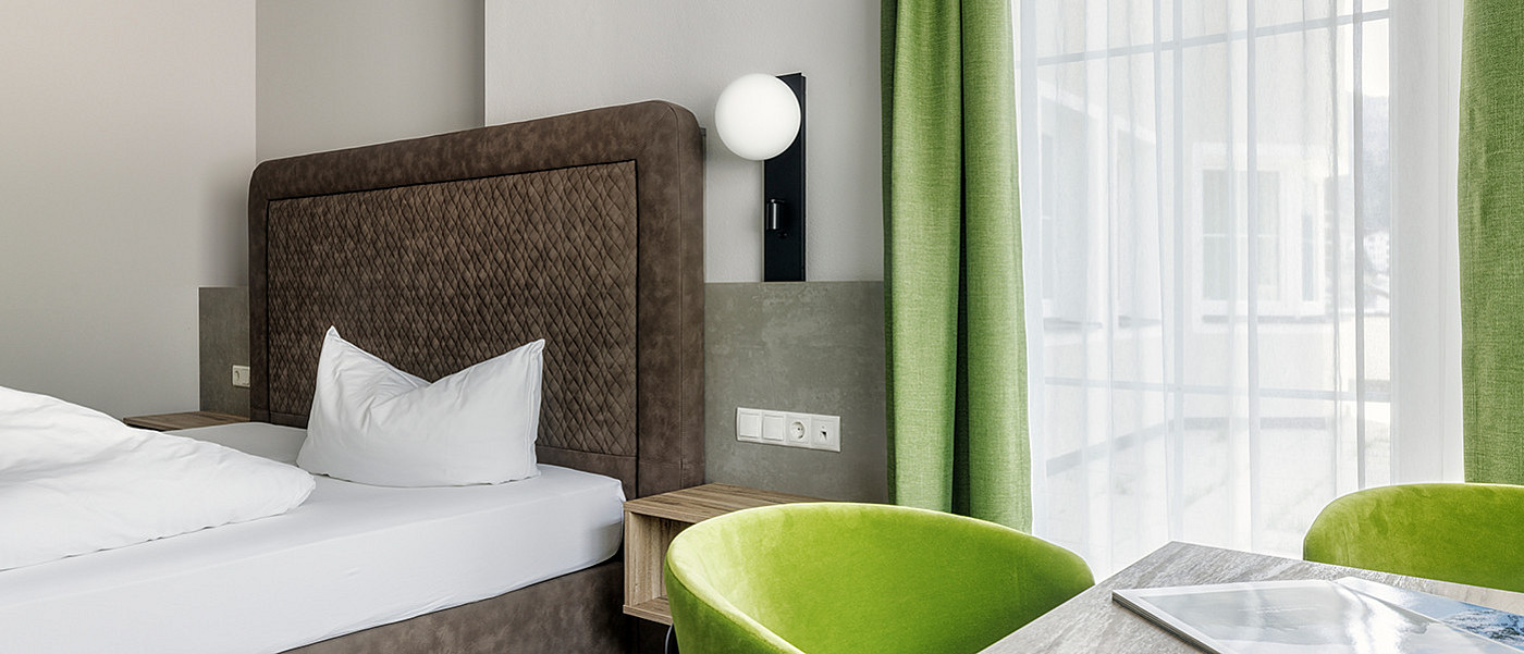 Cosy hotel room with table and green chairs.