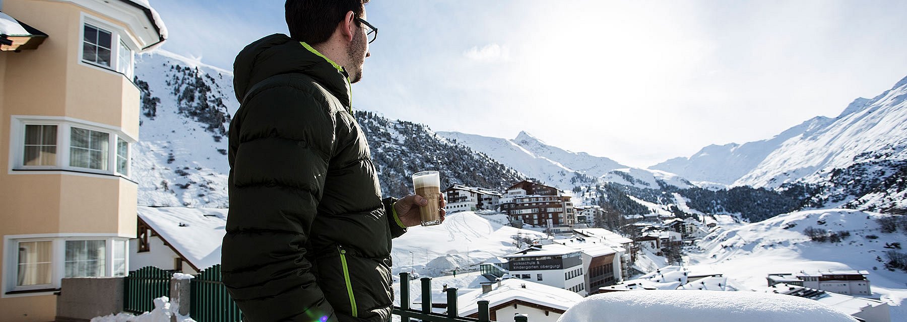 Mann auf Hotelterrasse vor verschneitem Bergpanorama