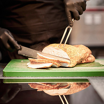 Ein Koch schneidet eine gekochte Hühnerbrust.