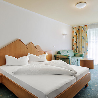 A sofa stands next to a double bed in a hotel room.