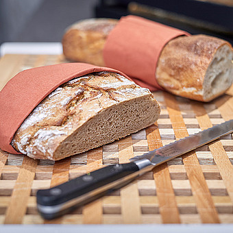 A loaf of bread and a knife lie on a wooden board.