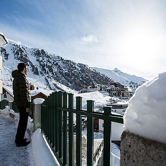 Ein Mann steht auf der Terrasse und blickt auf die verschneite Landschaft.