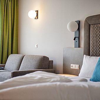 A small couch stands next to a large double bed.